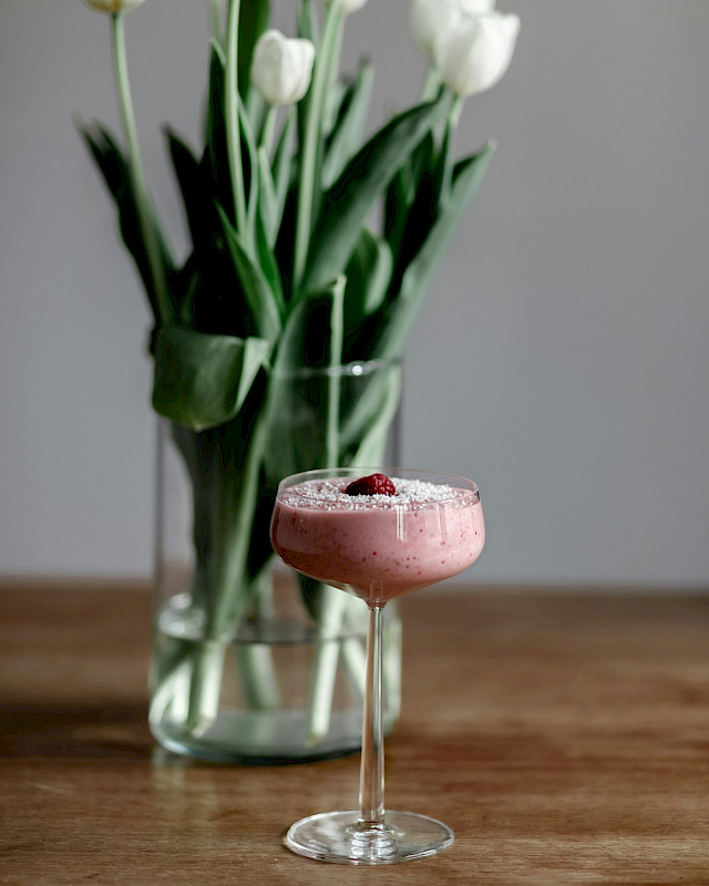 Розовый ягодный смузи с UNIQUE Pink Collagen в бокале рядом с белыми тюльпанами